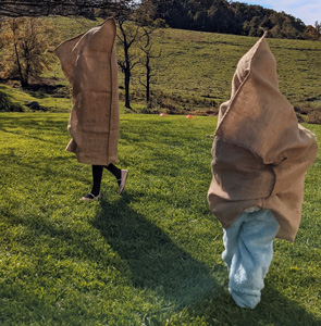 Child and adult jumping in burlap potato sacks during a sack race game